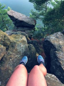 Alexandra's legs in blue tennis shoes as she sits on the edge of a rock formation over water. She is at a Wisconsin state park near her home.